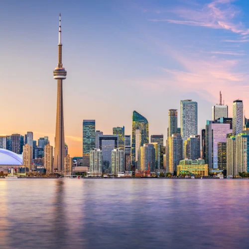 Toronto skyline at sunset with CN Tower and Rogers Centre reflected on Lake Ontario.