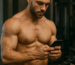 Muscular bodybuilder posing shirtless in a modern gym setting