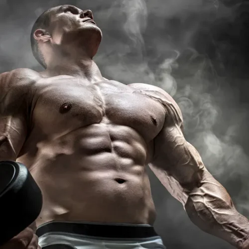 Strong male athlete holding dumbbells against a smoky background, upper body flexed.