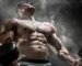 Strong male athlete holding dumbbells against a smoky background, upper body flexed.