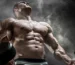 Strong male athlete holding dumbbells against a smoky background, upper body flexed.