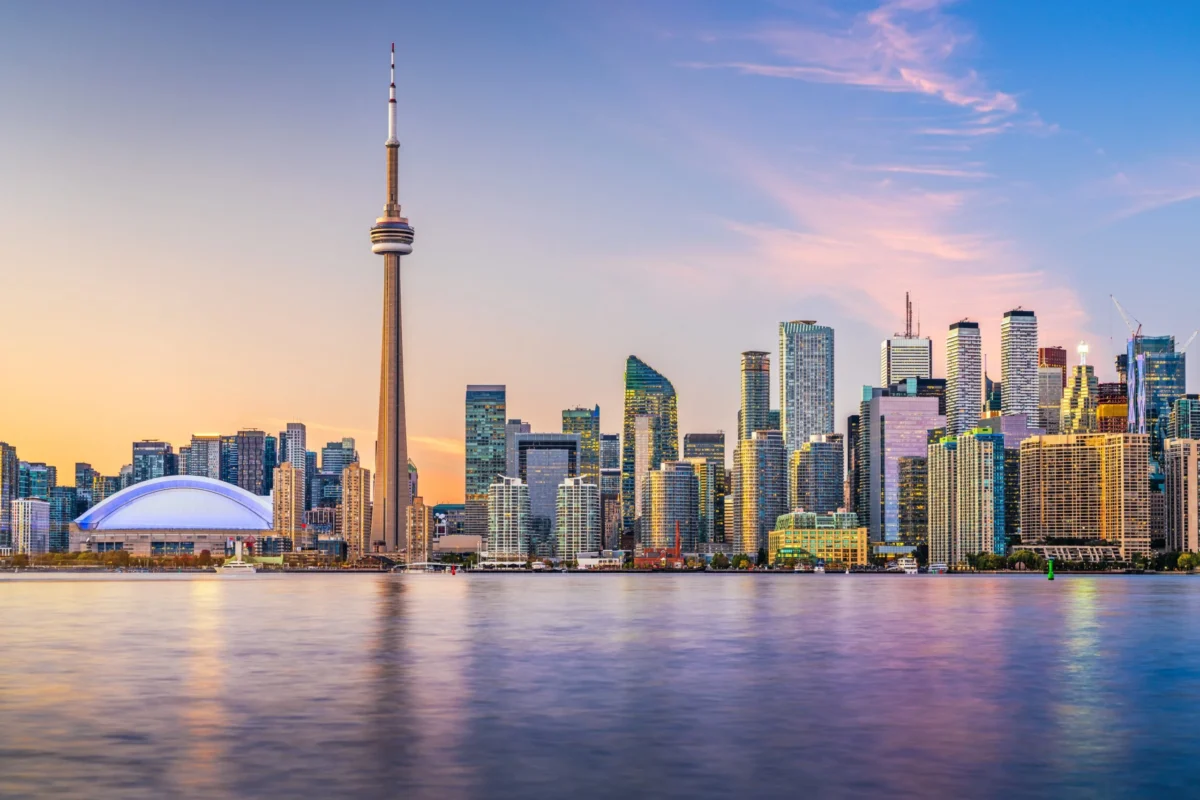 Toronto skyline at sunset with CN Tower and Rogers Centre reflected on Lake Ontario.